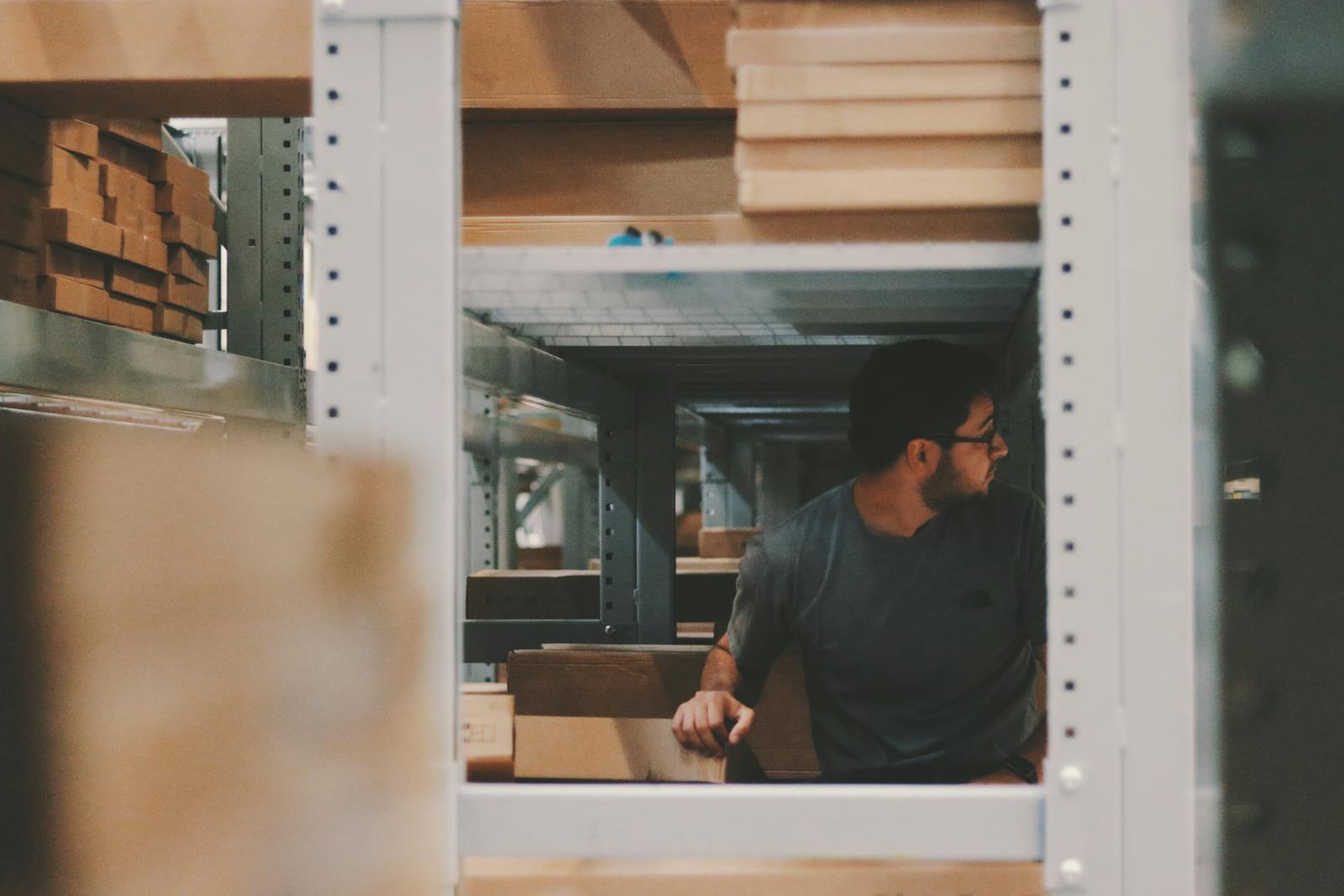 Man organizing wooden planks on warehouse shelves, creating an efficient storage solution.